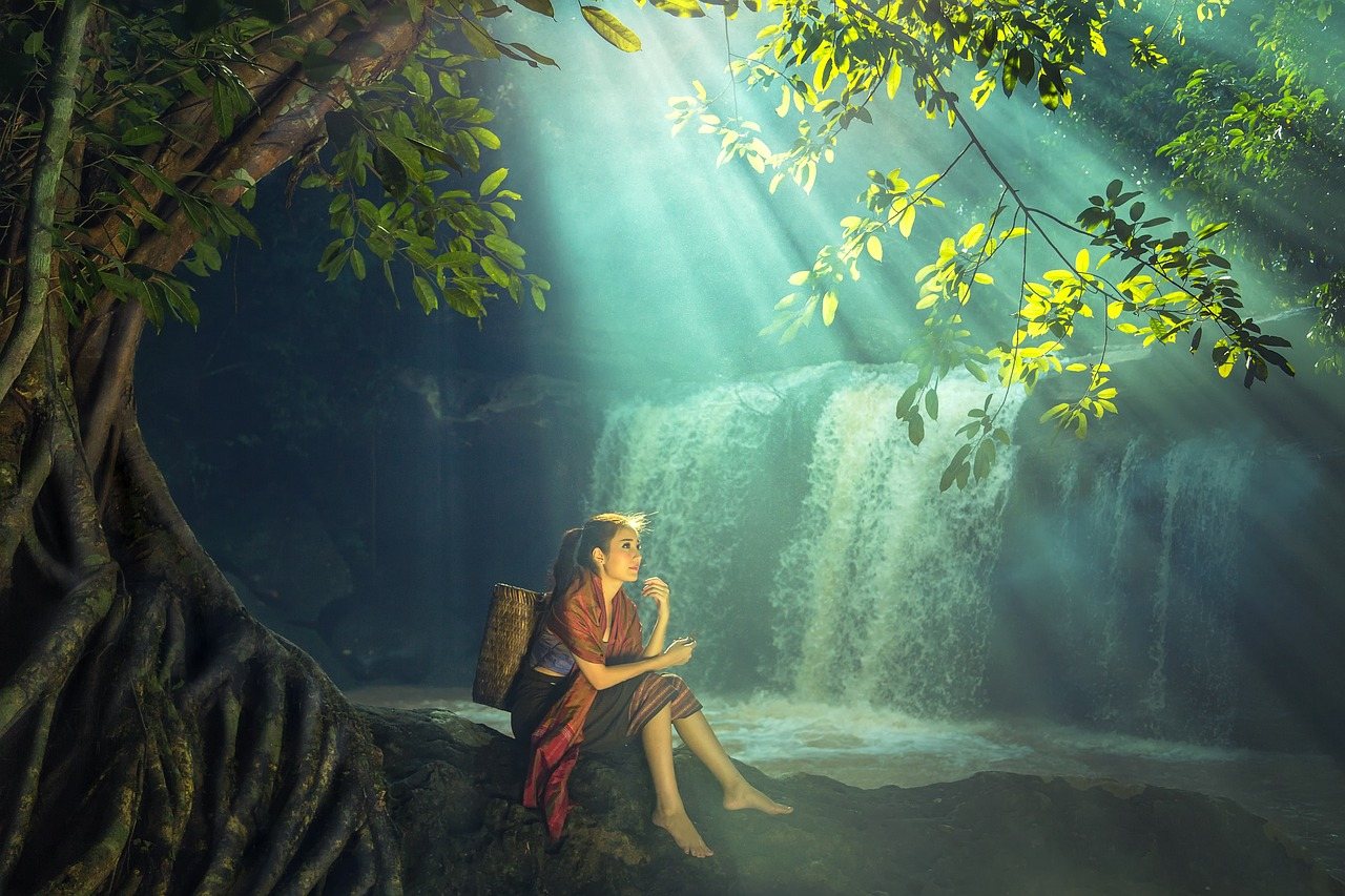 Lady sitting in peaceful forest jungle beside waterfall